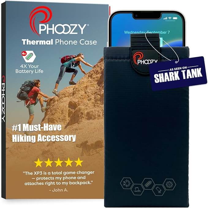 PHOOZY XP3 thermal phone case in black clipped to a snowboard jacket zipper with snow-covered mountain peaks visible in the background