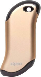 Zippo HeatBank 9s rechargeable hand warmer and power bank in silver, held in a gloved hand against a snowy mountain background with USB charging cable visible